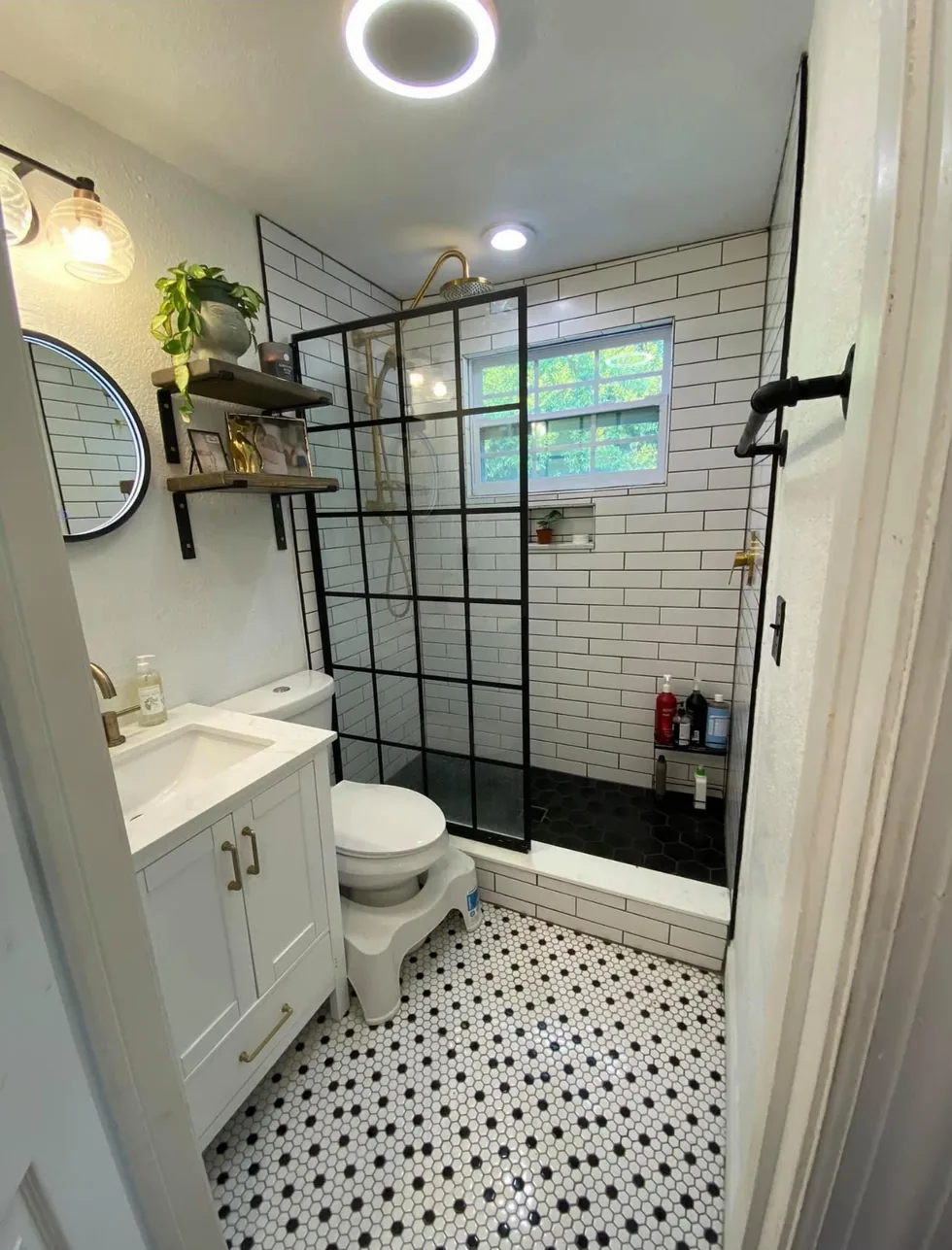 Bathroom after remodeling with white subway tile, black shower glass, brass fixtures, and mosaic floor tile.