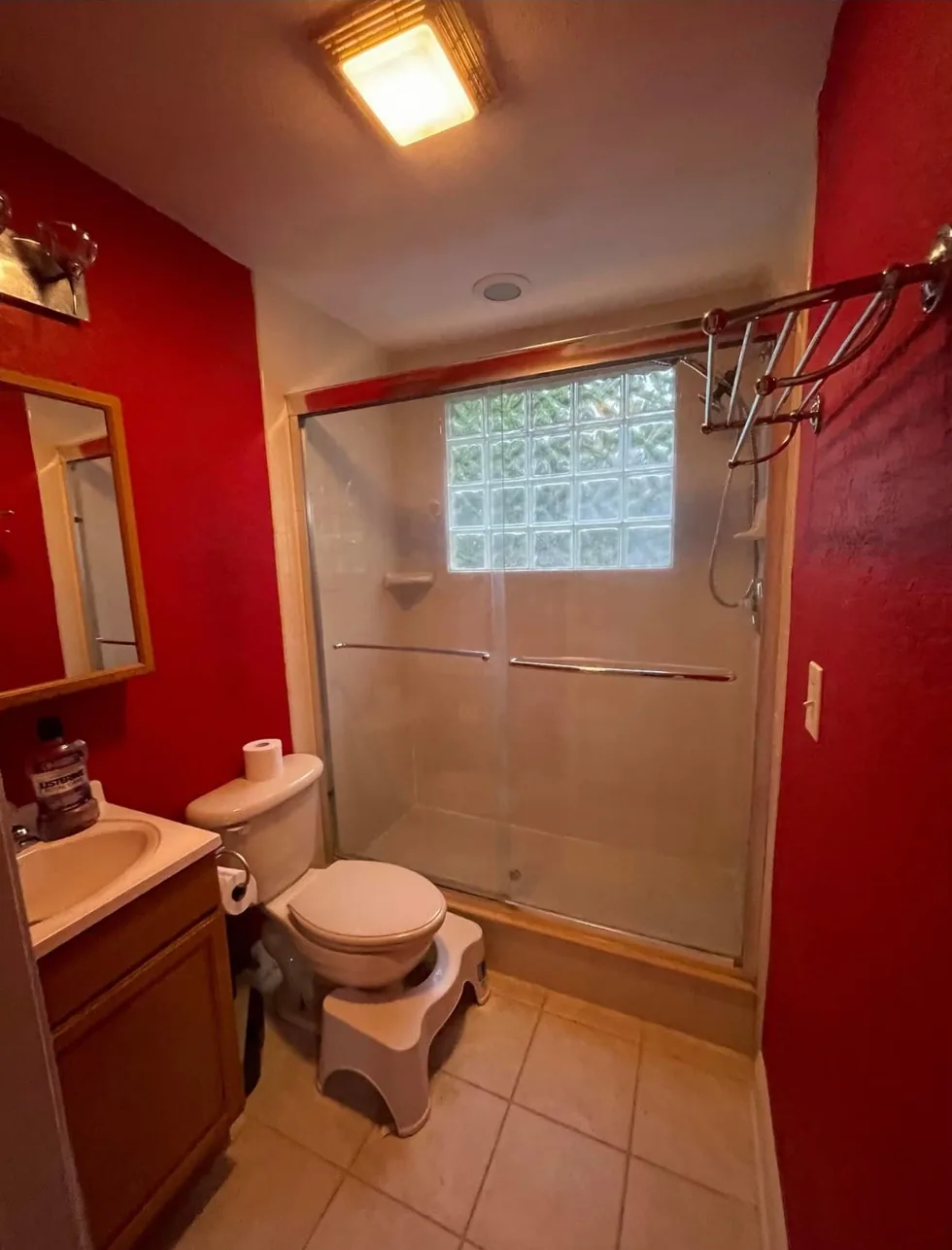 Bathroom before remodeling with red walls, dated tile, and an older shower enclosure.